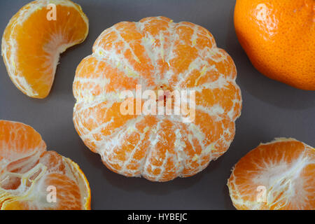 high angle view of a closeup of peeled and unpeeled whole mandarin and pieces on a grey background Stock Photo