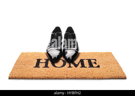 Pair of shoes on a doormat with the word home written on it isolated on white background Stock Photo
