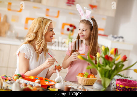 Young mother in kitchen with girl painting Easter eggs Stock Photo