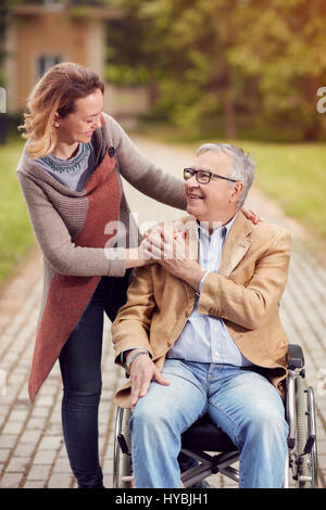 Smiling young woman with her disabled father on wheelchair in park Stock Photo