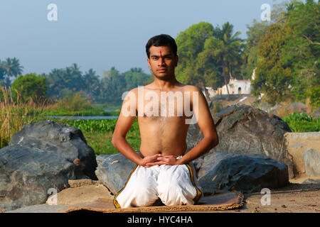 Indian man practicing yoga next to a river  in South India. Stock Photo