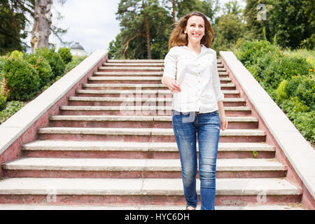 Happy young woman in white shirt descending stairs in park Stock Photo