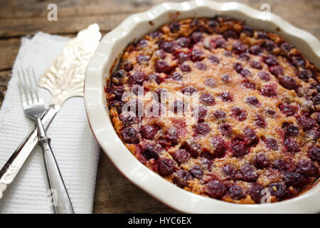 Cherry clafoutis pie in ceramic baking dish with spatula on wooden board Stock Photo