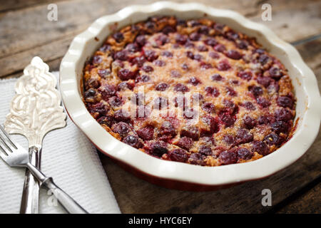 Cherry clafoutis pie in ceramic baking dish with spatula on wooden board Stock Photo