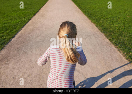 Beautiful child blond girl driving scooter on rural road outdoor in park Stock Photo