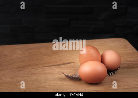 brown eggs on a wooden board with feathers set against a black background Stock Photo