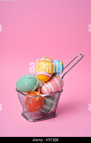 a pile of different decorated easter eggs in a metal basket against a pink background with a blank space on top Stock Photo