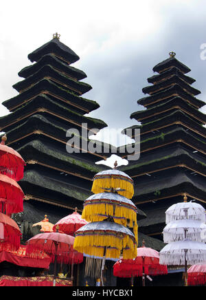 Two black hindu temple rooftop buildings with red yellow white colored umbrellas in front at the celebration day of Galungan in the afternoon, Bali In Stock Photo