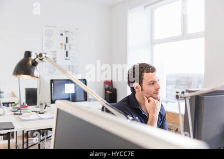 Mid adult man in office using computer hand on chin Stock Photo
