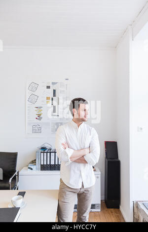 Mid adult man in office arms crossed looking sideways through window Stock Photo