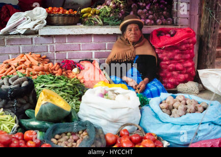 Indigenous woman at the vegetable market using coca leaf on her forehead to relieve headache. October 13, 2012 - Chulumani, Bolivia Stock Photo