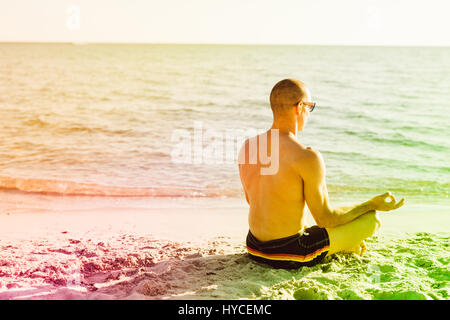 Young man doing yoga on the beach - meditation, relaxing, zen concept Stock Photo