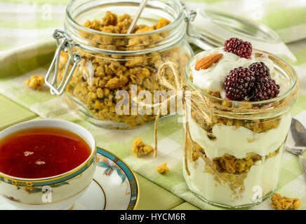 Healthy breakfast ingredients. Homemade granola with yoghurt in open glass jar and cup of tea. The food is rich in useful carbohydrates, vitamins and  Stock Photo