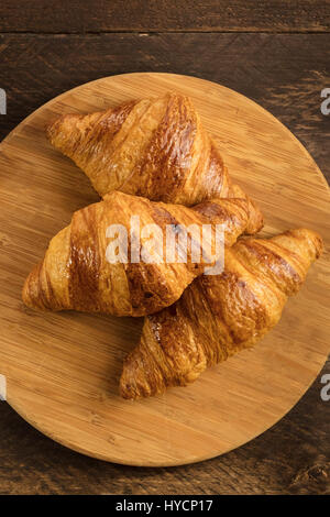 Three crunchy croissants on wooden board with copyspace Stock Photo