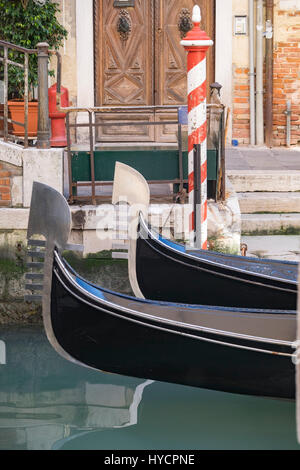 The prows of two gondolas moored at a landing on a canal in Venice with the traditional barber pole nearby. Stock Photo