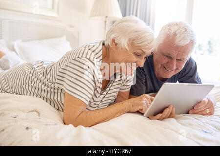 Happy senior couple lying in bed using a digital tablet Stock Photo