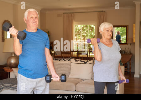 Active senior couple lifting dumbells together in their living room Stock Photo