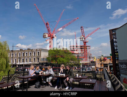 Young people sitting at a cafe by construction and housing building work of homes and offices by Regent's canal for the Camden Lock Village development in Camden,London,England,UK Stock Photo