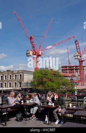 Young people sitting at a cafe by construction and housing building work of homes and offices by Regent's canal for the Camden Lock Village development in Camden,London,England,UK Stock Photo