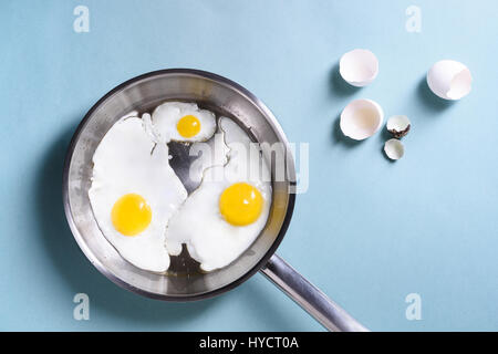 Healthy morning breakfast with fried eggs, over a blue table background. Chicken egg and quail egg in a pan. Top view, copy space, flat lay. Stock Photo