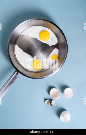 Fried eggs for breakfast in a cooking pan. Chicken egg, quail egg, yolk and egg shell. Top view, copy space. Flat lay. Stock Photo