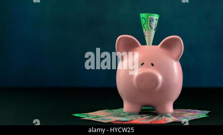 Pink Piggy bank money concept on dark blue background with Australian cash and a one hundred dollar note inserted. Stock Photo