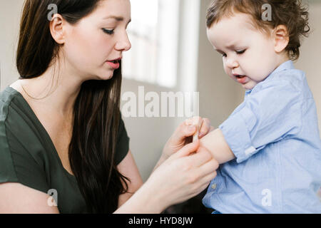 Mother applying plaster on son's (4-5) arm Stock Photo