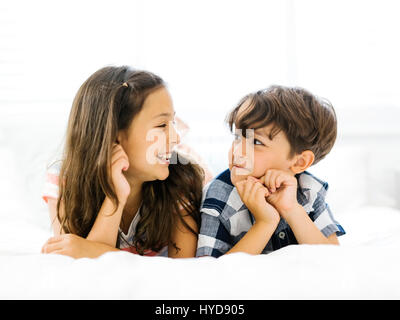 Siblings (10-11, 6-7) lying in bed side by side Stock Photo
