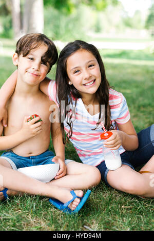 Boy (6-7) and girl (10-11) sitting on grass in summer Stock Photo
