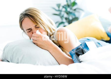 Young woman lying on bed and blowing nose Stock Photo