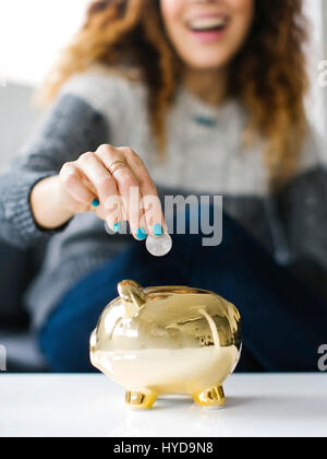 Woman dropping coin into gold piggy bank Stock Photo - Alamy