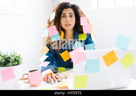 Woman covered with sticky notes using laptop at table Stock Photo