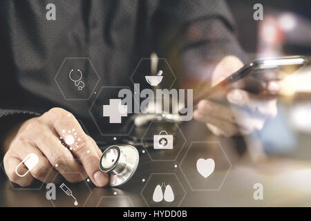 close up of smart medical doctor working with smart phone and stethoscope on dark wooden desk with virtual icon diagram Stock Photo