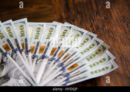 A stack of brand new one hundred dollar bills in US currency fanned out on a dark brown wooden table Stock Photo