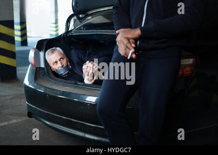 Successful assault. Nice calm adult man holding a cigarette and smoking it while enjoying leaning on the car boot Stock Photo