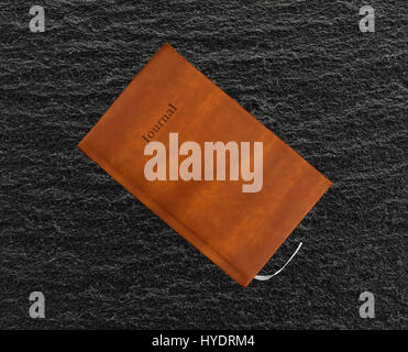 Top view of a brown leather journal on a black slate table. Stock Photo