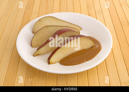 Slices of a red pear on a plate with peanut butter atop a wood plate mat. Stock Photo