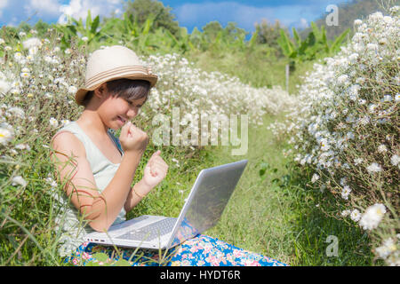 Asia teenage girl use laptop in Chrysanthemum field background sky blue. Stock Photo