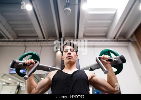 Hispanic man training in gym, doing machine shoulder press. Stock Photo