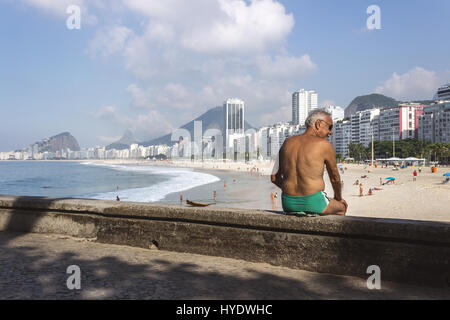 Brazil, Rio de Janeiro, Senior man seating on Leme beach with Copacabana on the background Stock Photo