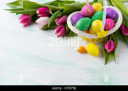 Easter multicolored glitter eggs in wicker basket and pink tulips background. Copy space. Happy Easter greeting card or invitation. Stock Photo