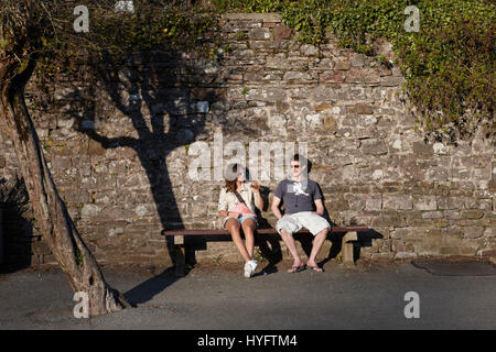 Couple Sitting on a bench in the sun on a bench reading a book at the Book Festival, Laugharne Stock Photo