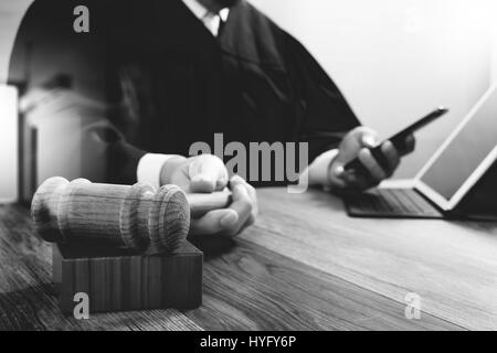 justice and law concept.Male judge in a courtroom with the gavel,working with digital tablet computer docking keyboard on wood table,black and white Stock Photo