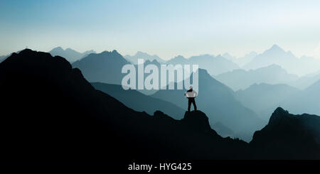 Spectacular mountain ranges silhouettes. Man reaching summit enjoying freedom. Stock Photo
