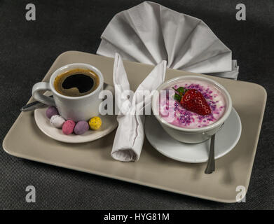 black coffee in a white cup, dessert, yogurt with a large strawberry and sprinkles, on a gray plate, napkin, sweet eggs, sweet set Stock Photo