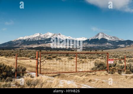 Snow capped mountain range on private property with a no trespassing sign. The driveway leads to an open field with a panoramic view of the mountains. Stock Photo