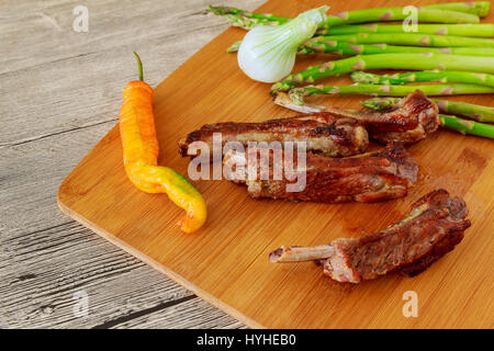 fresh glazed baked big beef meat rib chunk under sweet sauce with tomatoes hot chili pepper pink peppercorn and asparagus in black tray isolated on wh Stock Photo