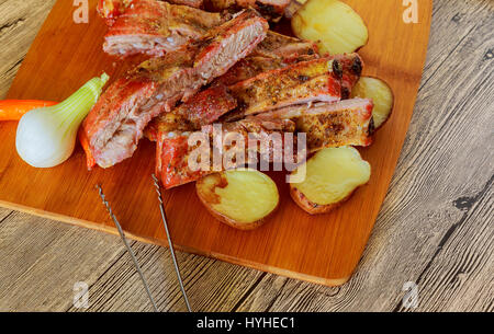 Delicious barbecued ribs seasoned with a spicy basting sauce and served with chopped fresh vegetables on an old rustic wooden chopping board in a coun Stock Photo
