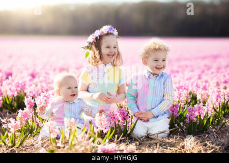 Three children playing in beautiful hyacinth flower field. Little girl, toddler boy and baby play in sunny summer garden with purple flowers. Kids hav Stock Photo