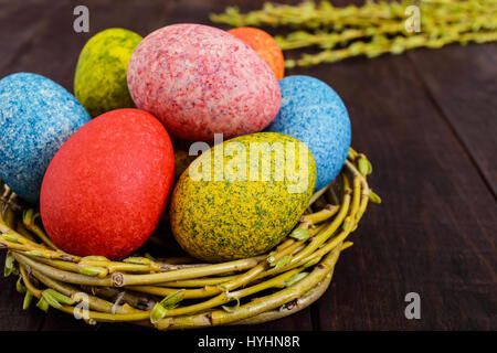 Colorful painted eggs in a nest of twigs of willow on a dark wooden background. Traditionally for Easter. Stock Photo